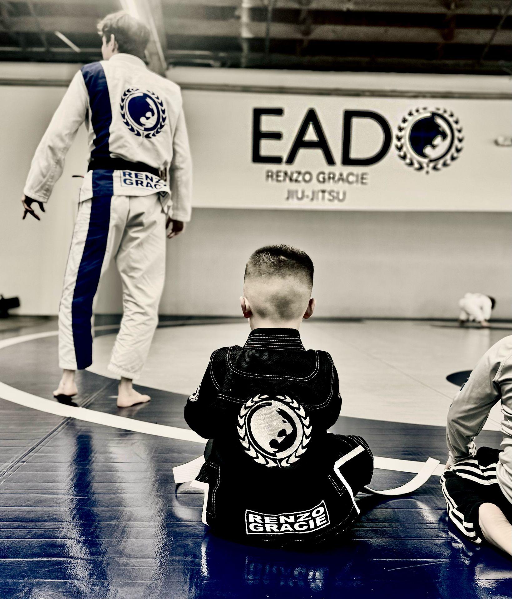 jiu jitsu class with child in gi and Renzo Gracie ado jiu jitsu logo on the wall