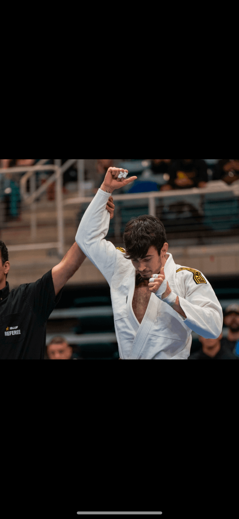 Victorious martial artist in white gi with referee raising his hand in celebration.